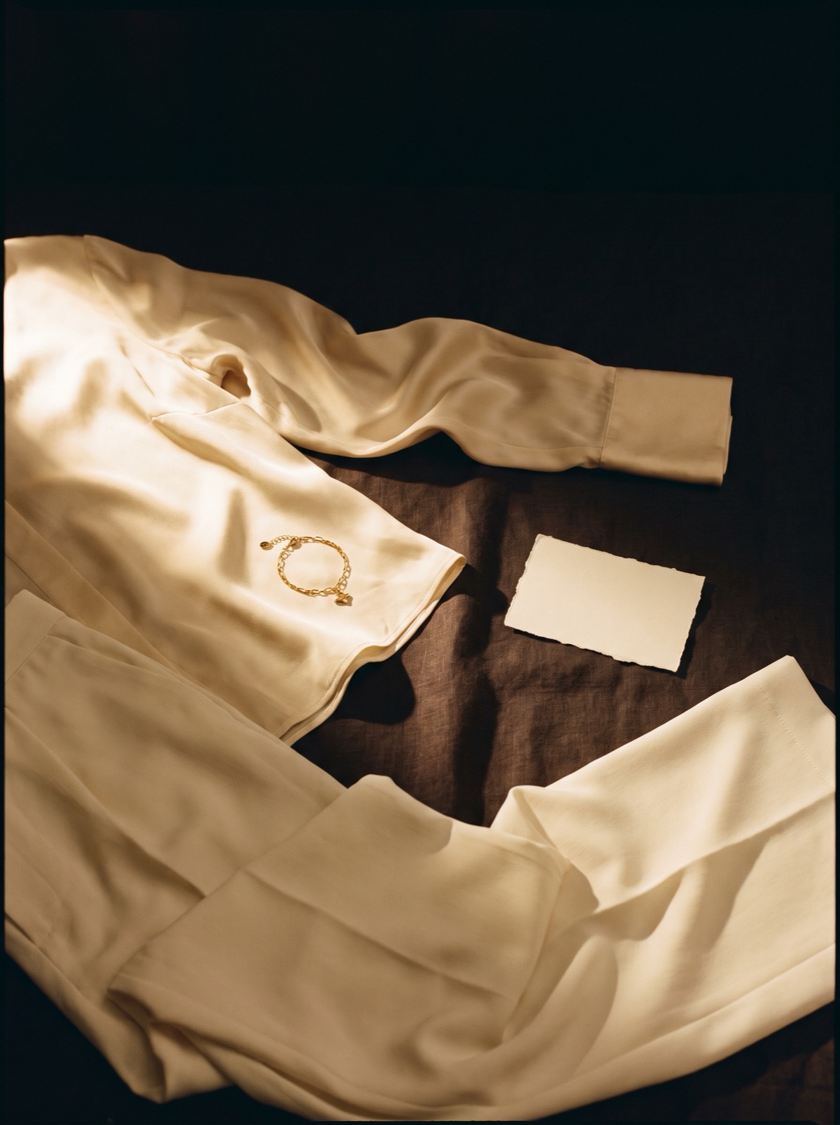 Cream silk laid out at night with a gold bracelet resting on it